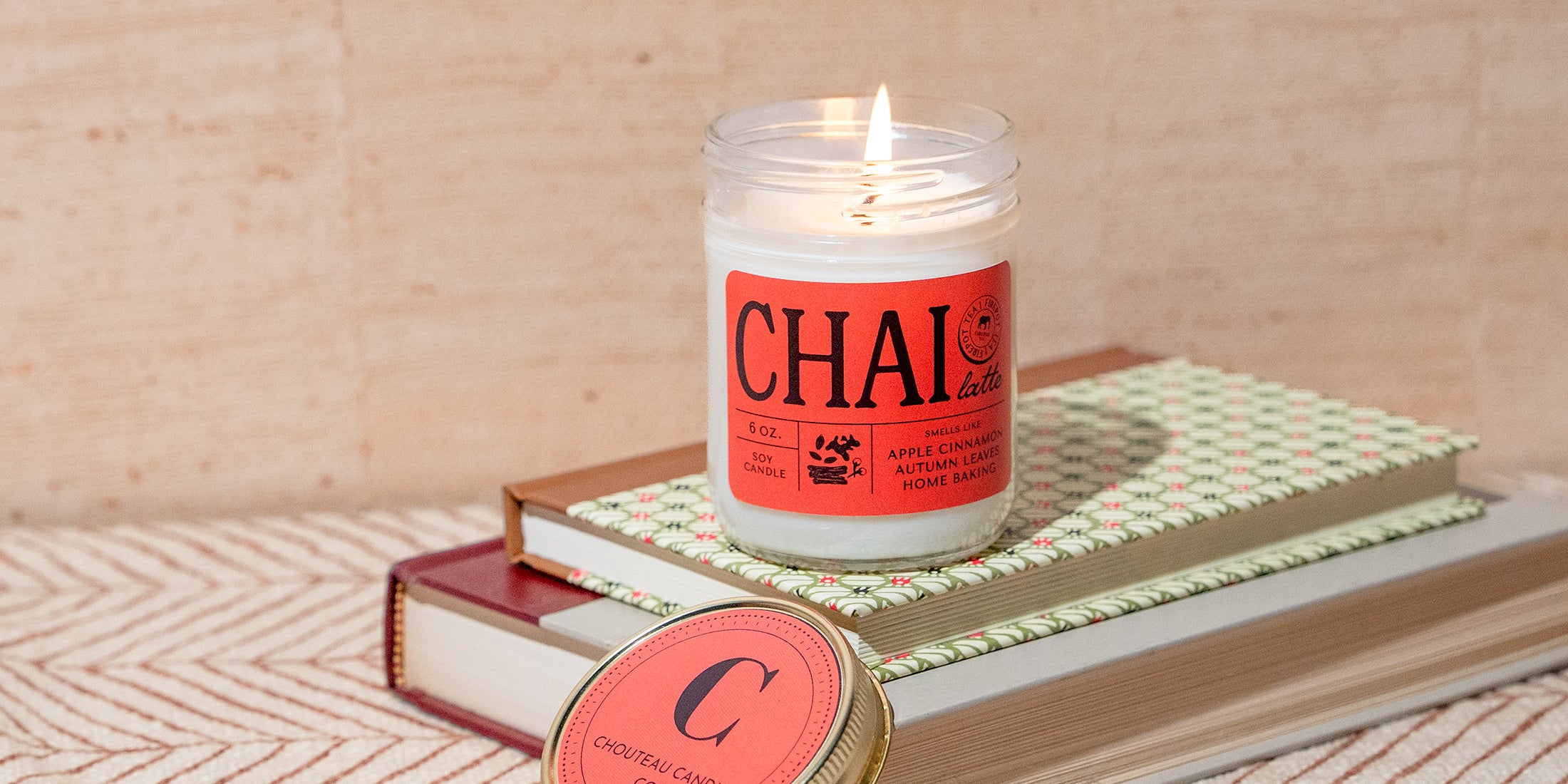 Candle with 'CHAI' label on a stack of books with a wooden background