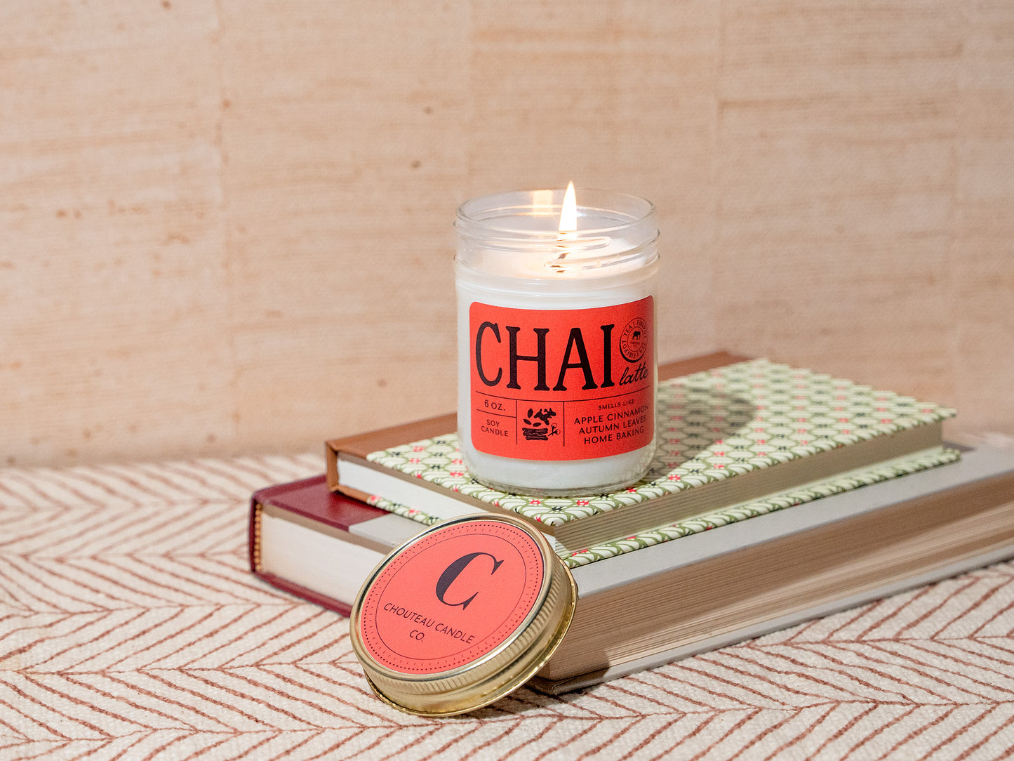Candle with 'CHAI' label on a stack of books with a wooden background
