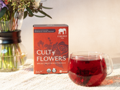 Box of 'Cult of Flowers' tea with a glass of red tea on a table.