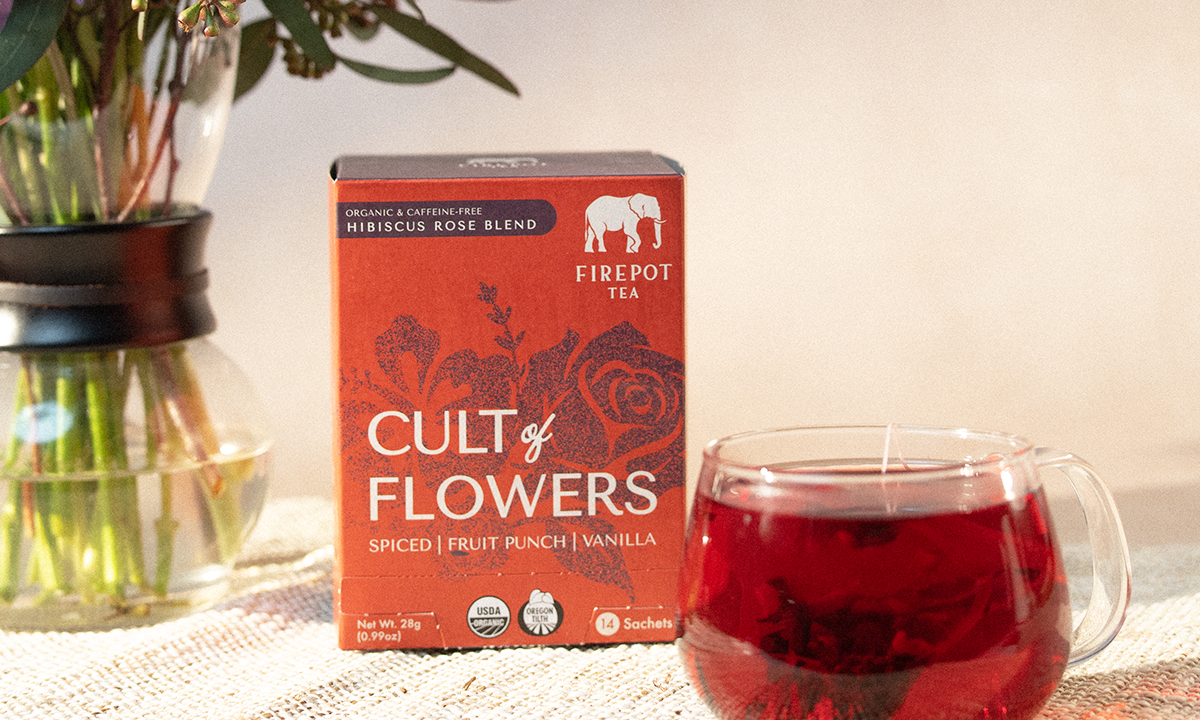 Box of 'Cult of Flowers' tea with a glass of red tea on a table.
