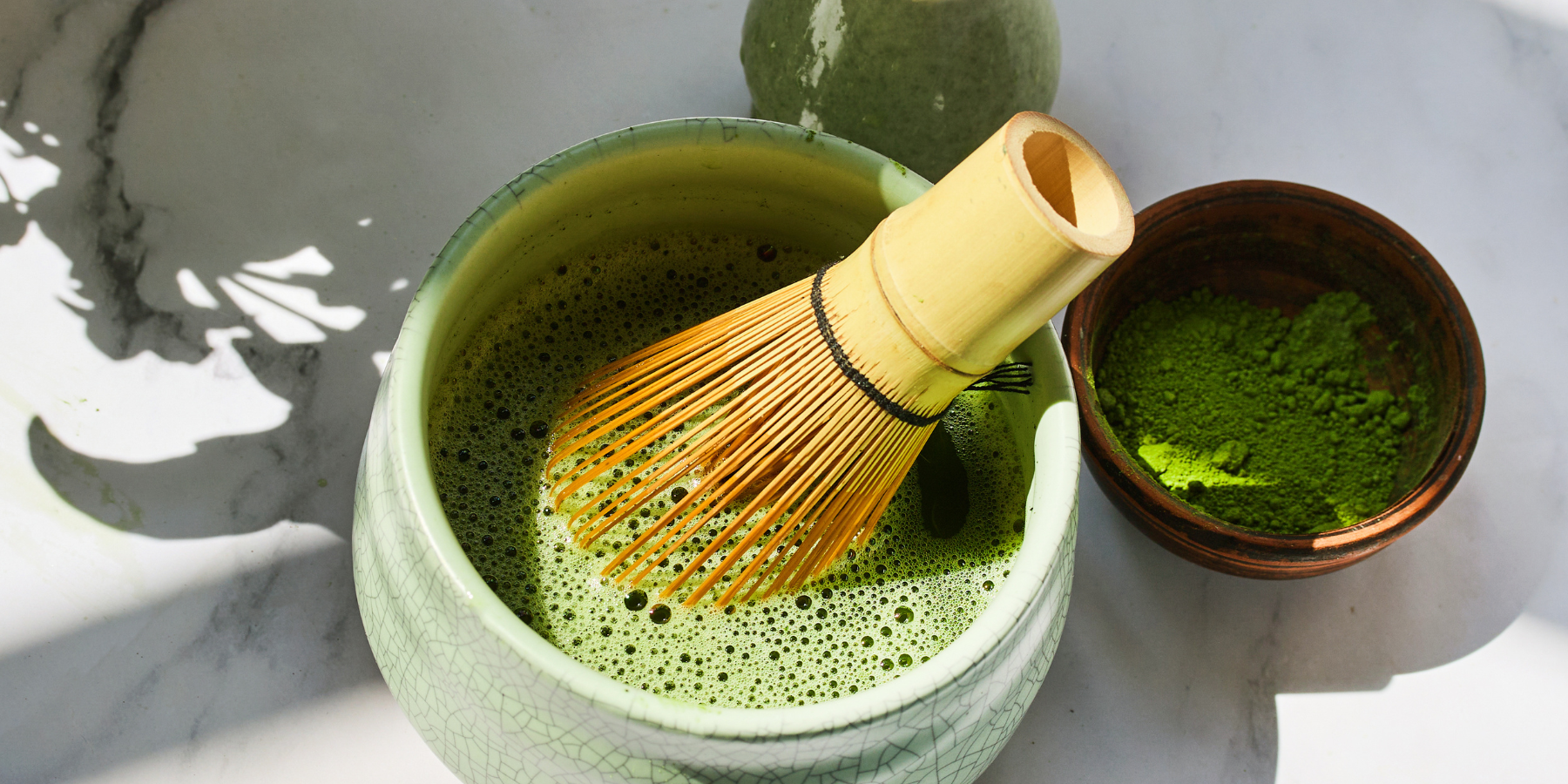 Matcha green tea preparation with a bowl, whisk, and container on a marble surface