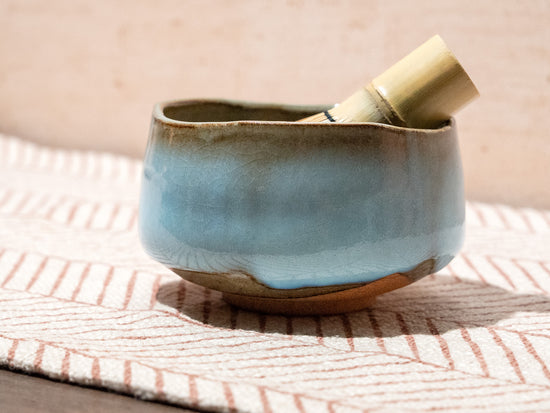Ceramic bowl with a bamboo whisk on a textured surface