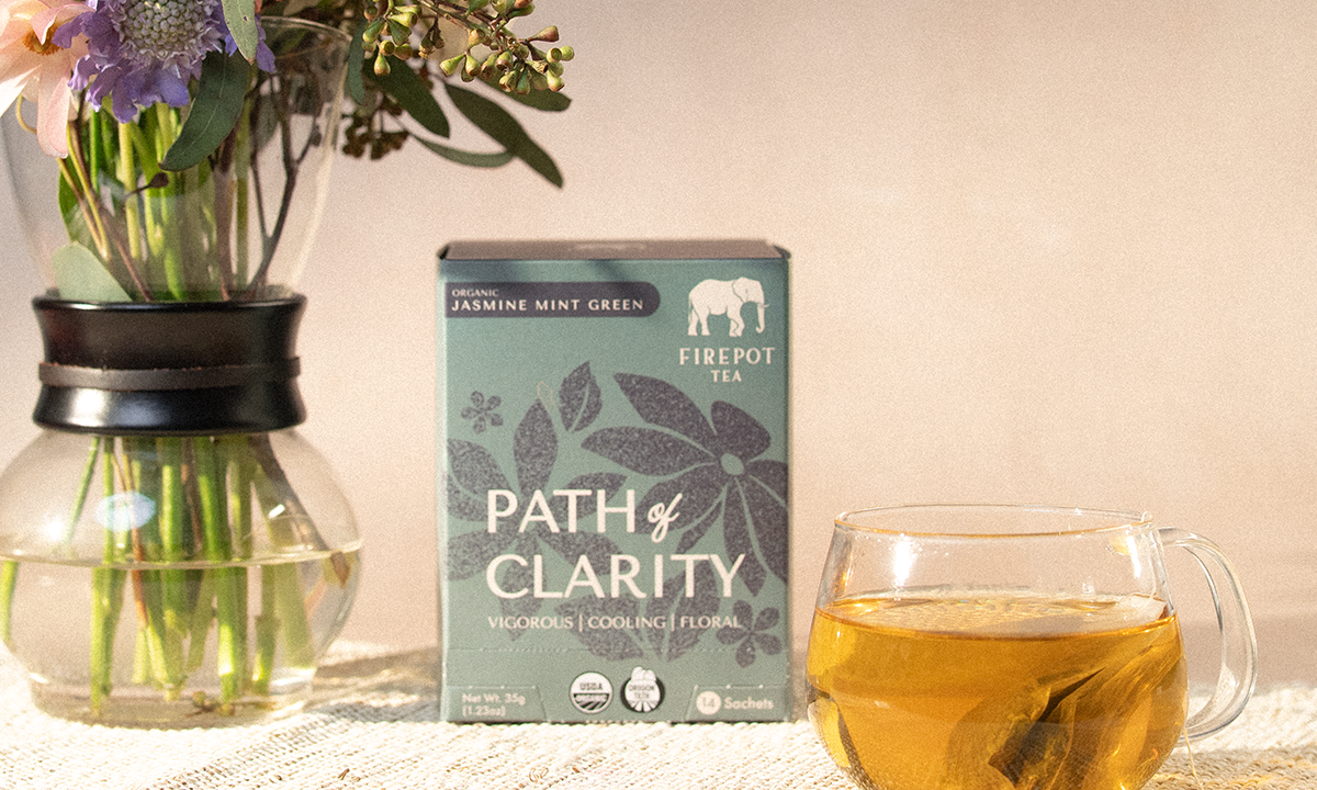 Tea box labeled 'Path of Clarity' with a glass of tea and flowers on a table.