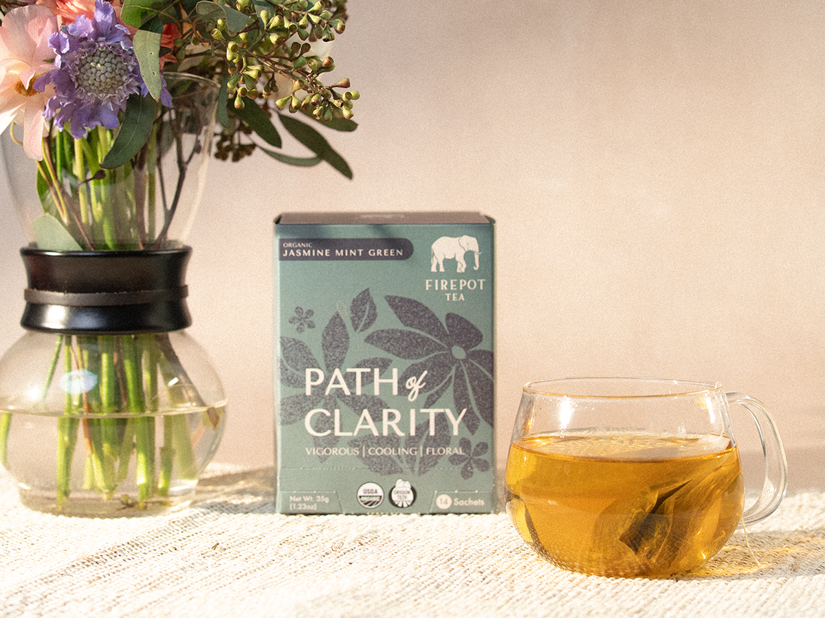 Tea box labeled 'Path of Clarity' with a glass of tea and flowers on a table.