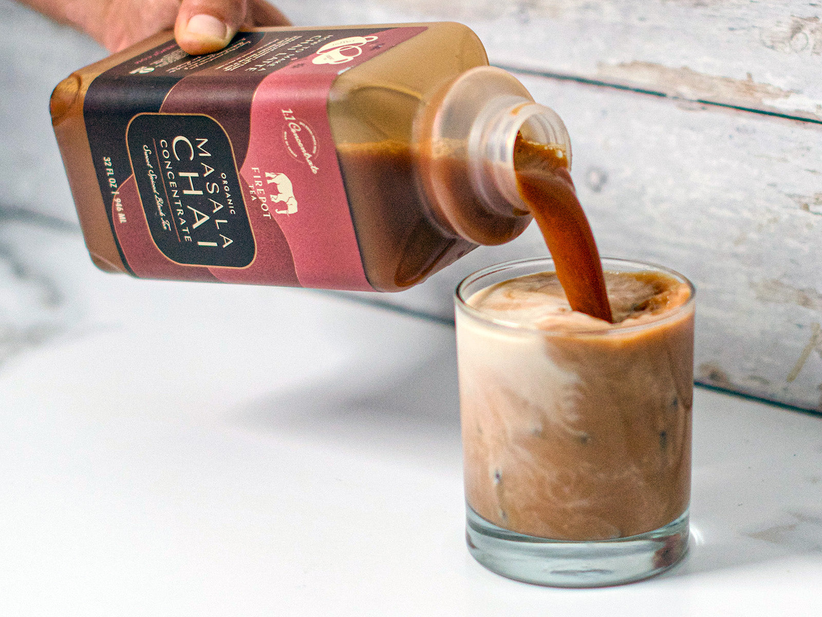 person pouring chai concentrate into a glass of milk