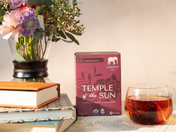 Firepot Tea 'Temple of the Sun' box with a glass of tea and flowers on a table.