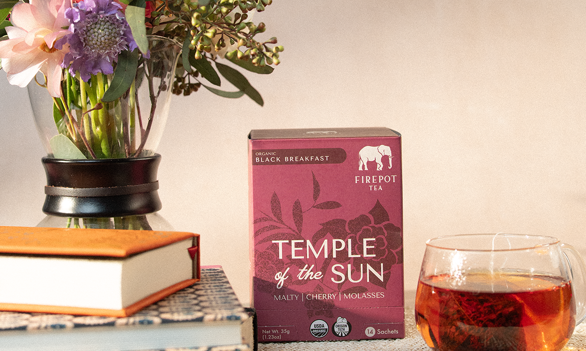Firepot Tea 'Temple of the Sun' box with a glass of tea and flowers on a table.