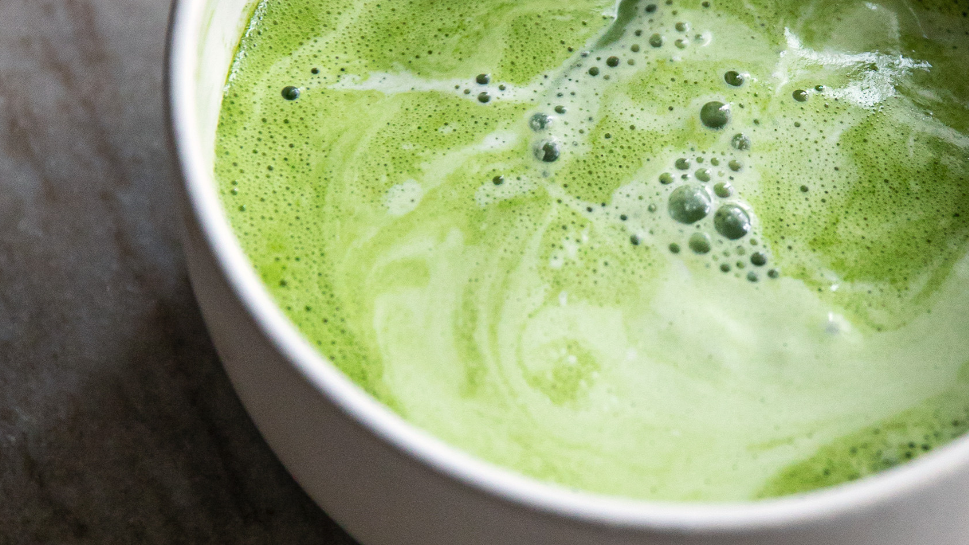Close-up of a green matcha latte in a white cup on a marble surface