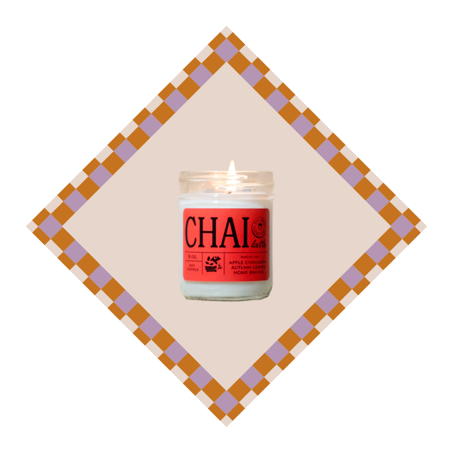 A lit white candle in a clear glass jar with a red label reading CHAI, centered inside a beige diamond with a brown and lavender checkered border on a white background.