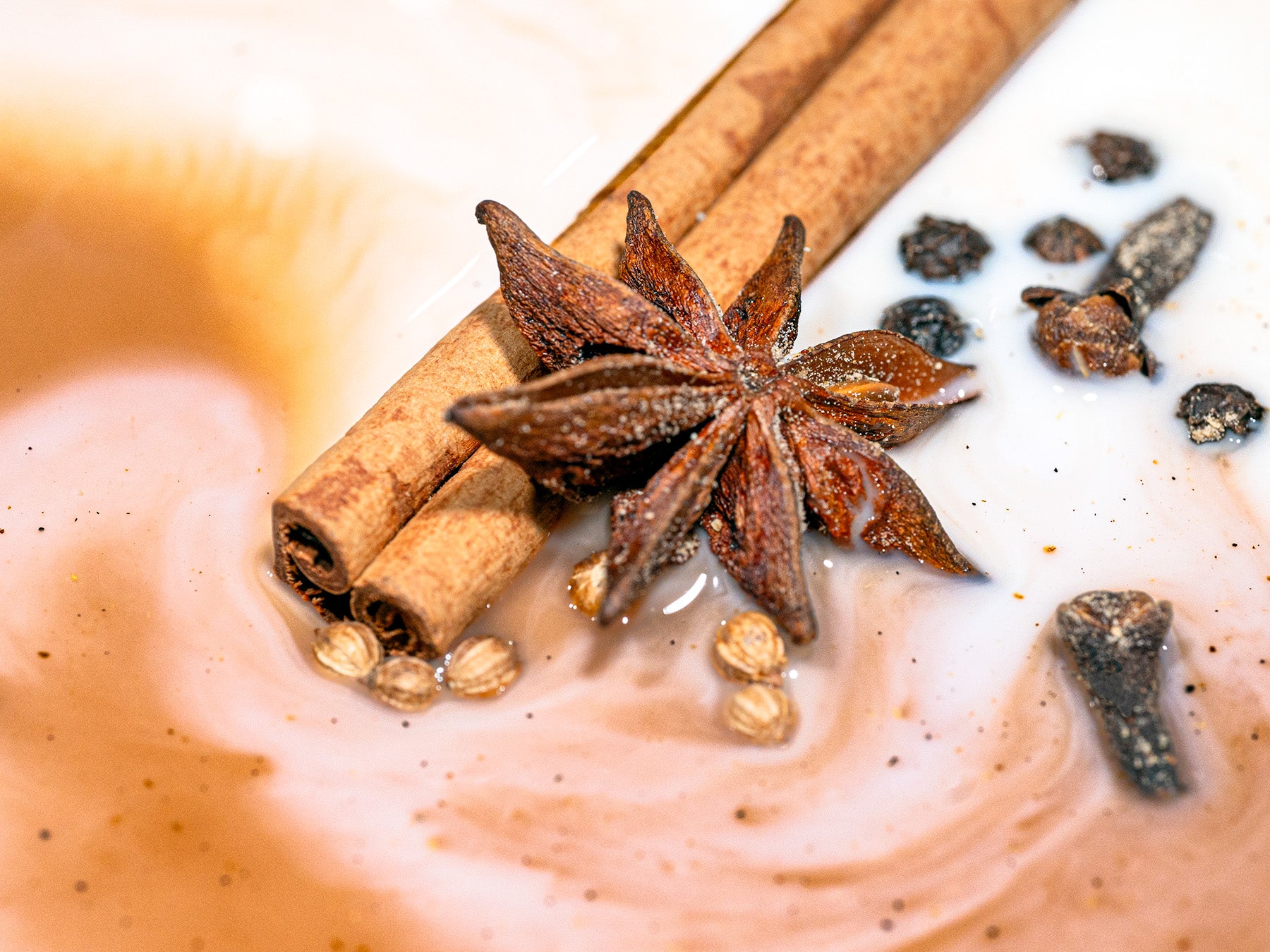 Spices including star anise, cinnamon sticks, and cloves on a creamy surface.