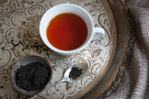 loose leaf Firepot Breakfast tea next to a teacup of steeped Firepot Breakfast tea