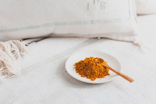 Golden Soul Turmeric powder with a wooden spoon on a white plate. 