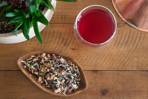 loose leaf Hibiscus Elixir tea next to a plant and a steeped cup of Hibiscus Elixir tea