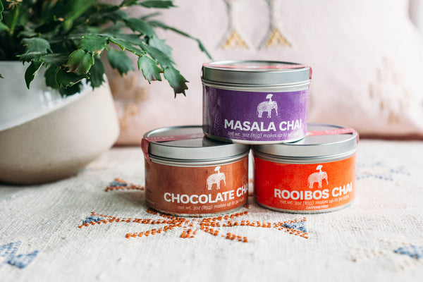 Firepot Masala Chai tin, Firepot Rooibos Chai tin, Firepot Chocolate Chai tin stacked in a pyramid, next to a plant