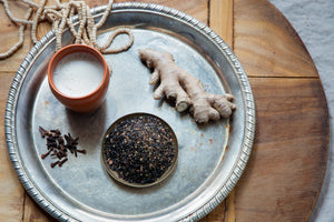 Firepot loose leaf Masala Chai next to a chai latte in a cup and a ginger root