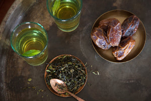 loose leaf Moroccan Jasmine Mint tea next to medjool dates and two cups of steeped Moroccan Jasmine Mint tea