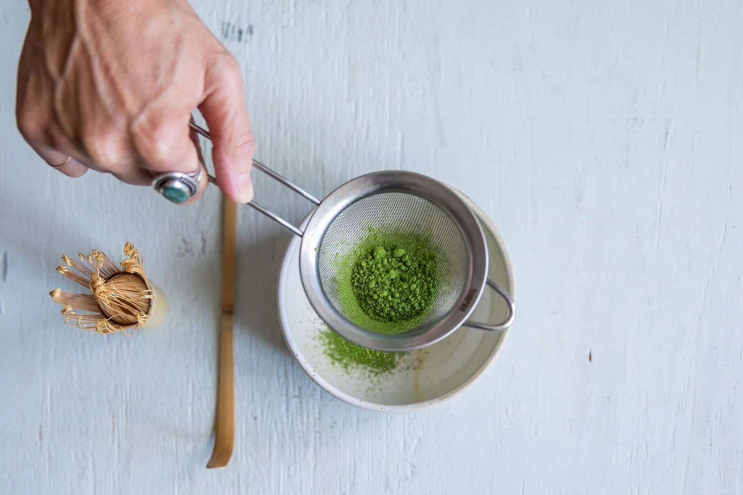 Load image into Gallery viewer, woman&amp;#39;s hand straining ceremonial matcha through a stainless steel strainer into a cup
