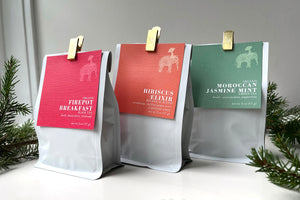 Firepot Breakfast tea, Hibiscus Elixir tea, and Moroccan Jasmine Mint tea lined up, surrounded by evergreen branches